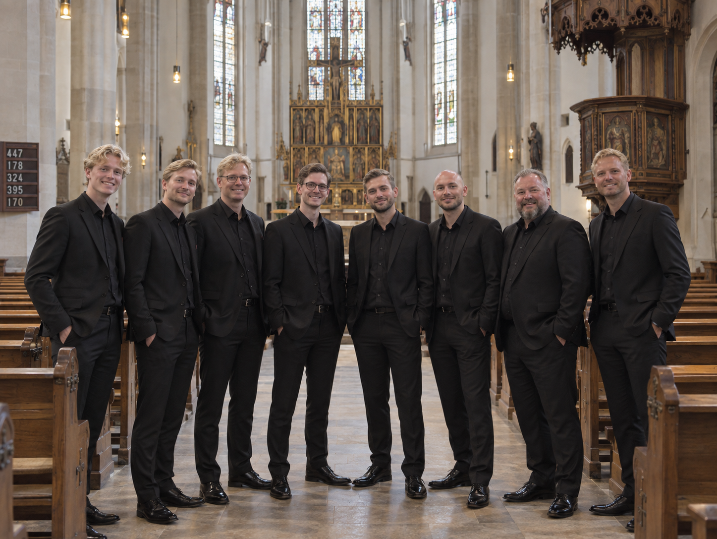 Die acht Sänger des Männerensembles in schwarzen Anzügen in einem Kirchenraum.